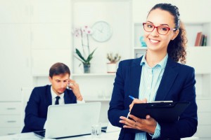 charming young woman manager holding cardboard and smiling in office